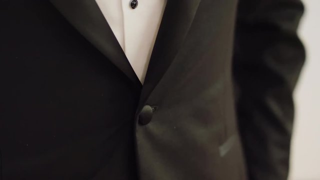 Groom Man in Festive White Shirt Fastens his Elegant Black Tuxedo on Button. Close Up Static 4K Stock Video Shot