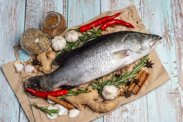 Fresh Raw Sea Bass on wooden table surrounded by fresh ingredients and spices.