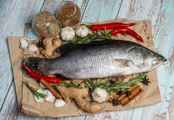 Fresh Raw Sea Bass on wooden table surrounded by fresh ingredients and spices.
