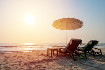 Sun umbrellas and chairs on tropical beach with sunset