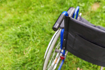 Empty wheelchair standing on grass in hospital park waiting for patient services. Invalid chair for...