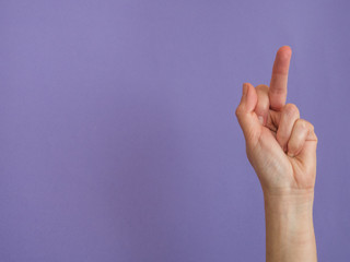 Hand showing middle finger on purple background with copy space
