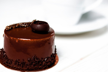 A delicious chocolate cake with chocolate pieces lies on a wooden stand next to a white cup, which stands on a white table