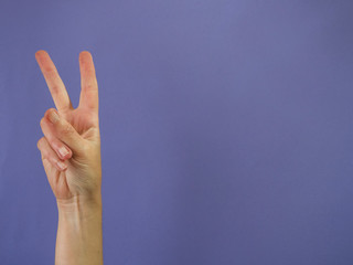 Hand with two fingers raised on purple background and copy space