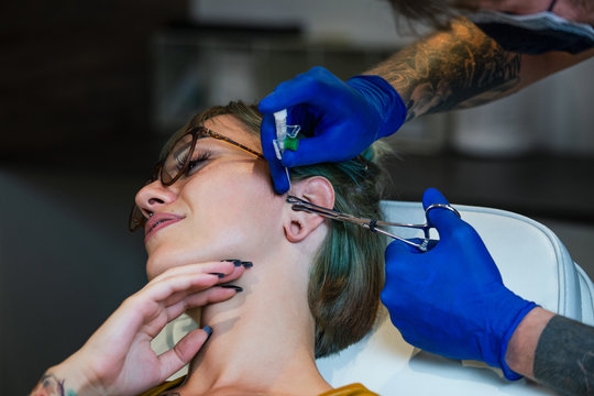 Portrait of a woman getting her ear pierced. Man showing a process of piercing ear with steril neadle and latex gloves. Ear Piercing Procedure