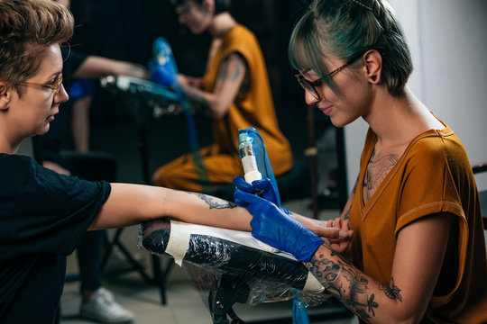 Tattoo Artist Demonstrates The Process Of Getting Black Tattoo With Paint. Portrait Of A Woman Tattoo Master Showing A Process Of Creation Tattoo On A Hand