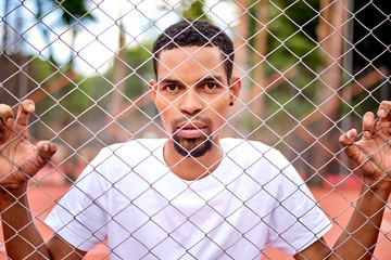 Black basketball player holding the chain link fence with hands