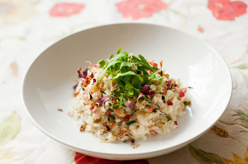 delicious italian homemade risotto on table cloth with arugula salad lemon and edible flowers and soft natural light