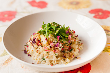 close up of delicious italian homemade risotto on table cloth with arugula salad lemon and edible flowers and soft natural light