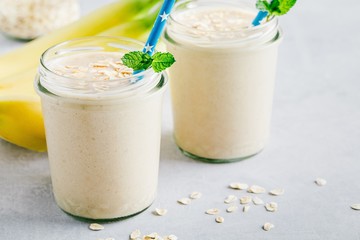 Banana oats smoothie or milkshake in glass mason jars on a stone background