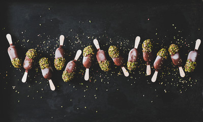 Ice cream popsicle pattern. Flat-lay of chocolate glazed ice cream pops with pistachio icing over...