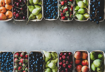 Summer fruit and berry variety. Flat-lay of ripe strawberries, cherries, grapes, blueberries, pears, apricots, figs in wooden eco-friendly boxes over grey background, top view, copy space