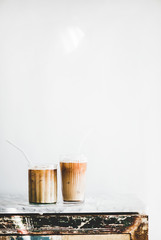 Homemade iced latte coffee in glasses with straws on grey marble table, white wall at background, copy space, vertical composition. Summer cold refreshing drink concept