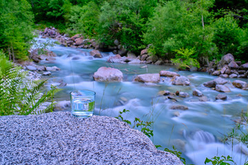 Glass with water in the background of a mountain river. Photo taken at long exposure.