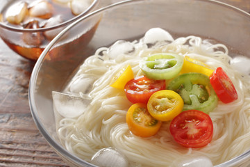 ミニトマトを乗せたガラスの透明な器に入った木目板の上のそうめん