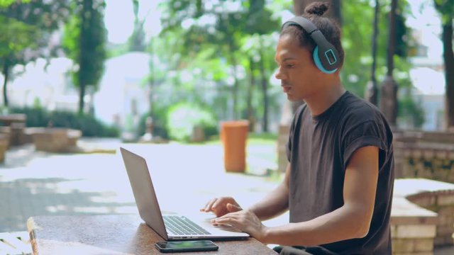 handsome mixed race composer beats rhythm composes music track looking on screen laptop outdoors, handsome freelancer work remote summer city landscape