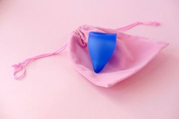 lue menstrual cup and bag on pink background. Feminine hygiene alternative product instead of...