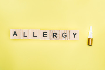 top view of wooden blocks with allergy lettering near nasal spray isolated on yellow