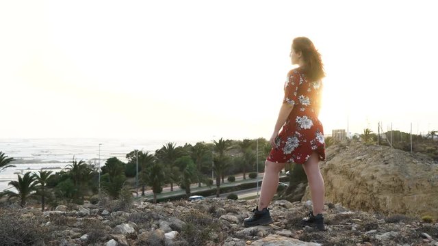 Girl with red dress. Cliff and city coast views at sunset. Almerimar, Almeria, Spain