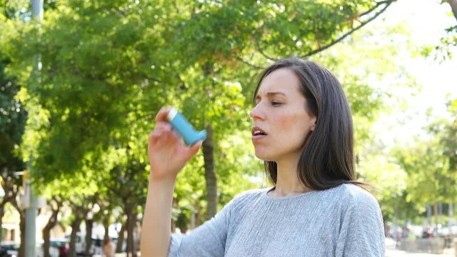 Adult asmathic woman suffering asthma attack using inhaler in a park