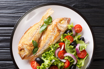 Tasty fried pink dorado or gilt-head bream fish with vegetable salad close-up on a plate. Horizontal top view