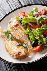 fried pink dorado served with lemon and fresh vegetables close-up on a plate on the table. vertical