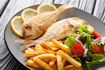 Freshly made pink dorado fish with french fries, lemon and vegetable salad close-up on a plate. horizontal