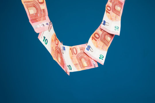 Billetes de dinero colgados de una cuerda por clips met&aacute;licos sobre fondo azul oscuro. Billetes de Euro en forma de collar en una cuerda