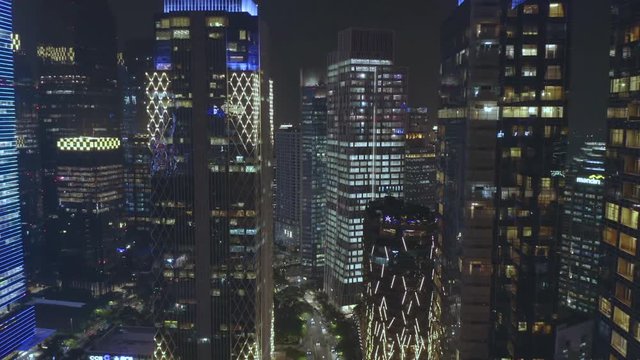 JAKARTA, Indonesia - July 15, 2019: Aerial scenery of dense modern office buildings with beautiful night lights in business center. Shot in 4k resolution from a drone flying forwards