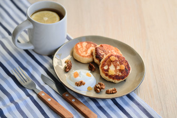 Close-up of homemade cheese pancakes syrniki with sour cream and cup of tea