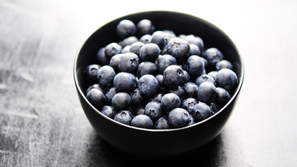 Freshly picked blueberries in black bowl on dark background.