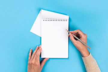 Obraz premium Woman's hands with perfect manicure holding pencil and notepad as mockup for your design. blue background, flat lay style.