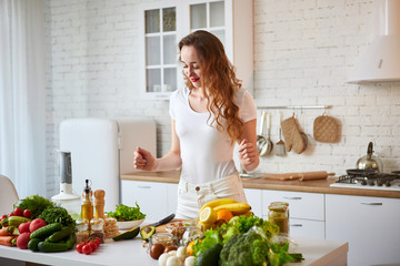 Young happy woman preparing tasty salad in the beautiful kitchen with green fresh ingredients...