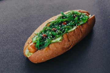 Big hotdog with sausage tomatoes, mustard and salad isolated on black background.