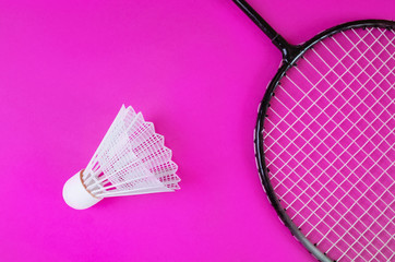 A shuttlecock and badminton racket on a bright pink background. Copy space. Amateur accessories for playing badminton. Flat lay, minimalism, top view.