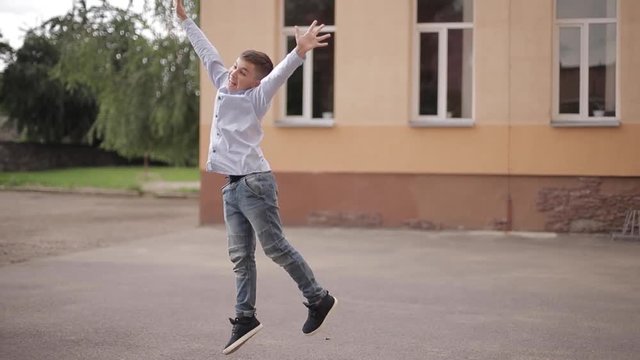 Happy boy jump and raises hands up. Background of school