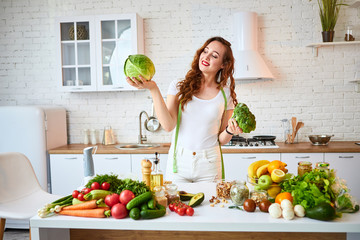 Young happy woman holding broccoli and cabbage in the beautiful kitchen with green fresh...