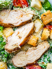 Classic Caesar salad with grilled chicken breast, parmesan cheese, tomatoes, lettuce. Close up Top view, space.