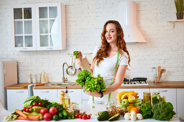 Young happy woman holding lettuce leaves for making salad in the beautiful kitchen with green fresh ingredients indoors. Healthy food and Dieting concept. Loosing Weight