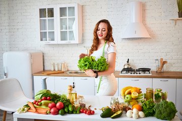 Young happy woman holding lettuce leaves for making salad in the beautiful kitchen with green fresh ingredients indoors. Healthy food and Dieting concept. Loosing Weight