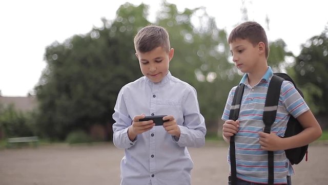 Two boys plays online games after school classes. Young boys smile and use phone
