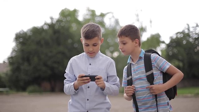 Two boys plays online games after school classes. Young boys smile and use phone