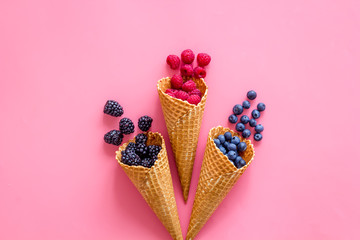 Fresh berries in waffle cones on pink background top view