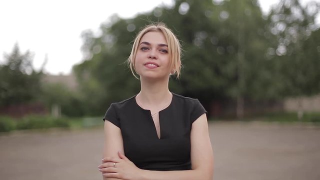 Young attractive female techer in black dress with sunglasses standing outside. Background of school