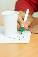 teenager writes marker chemical formulas on a white sheet with a glass of water