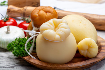 Italian provolone or provola caciocavallo hard and smoked cheeses in teardrop form served on olive tree board close up