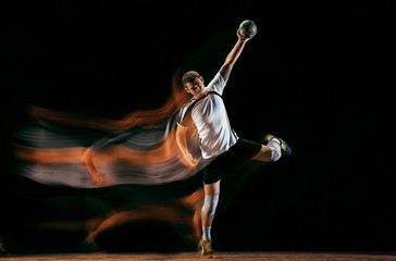 Obraz premium Caucasian young handball player in action and motion in mixed lights over black studio background. Fit male professional sportsman. Concept of sport, movement, energy, dynamic, healthy lifestyle.