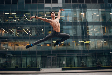 Young male ballet dancer jumping on a building background. Outdoor dance.