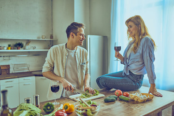 Happy couple cooking healthy food and drinking red wine at house kitchen.