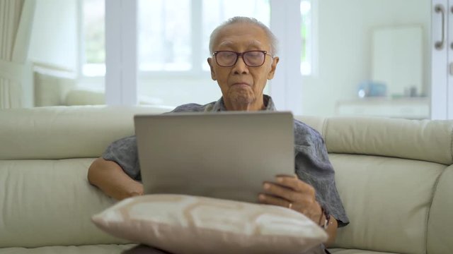 Portrait of senior man using a laptop computer while sitting on the sofa in living room at home. Shot in 4k resolution